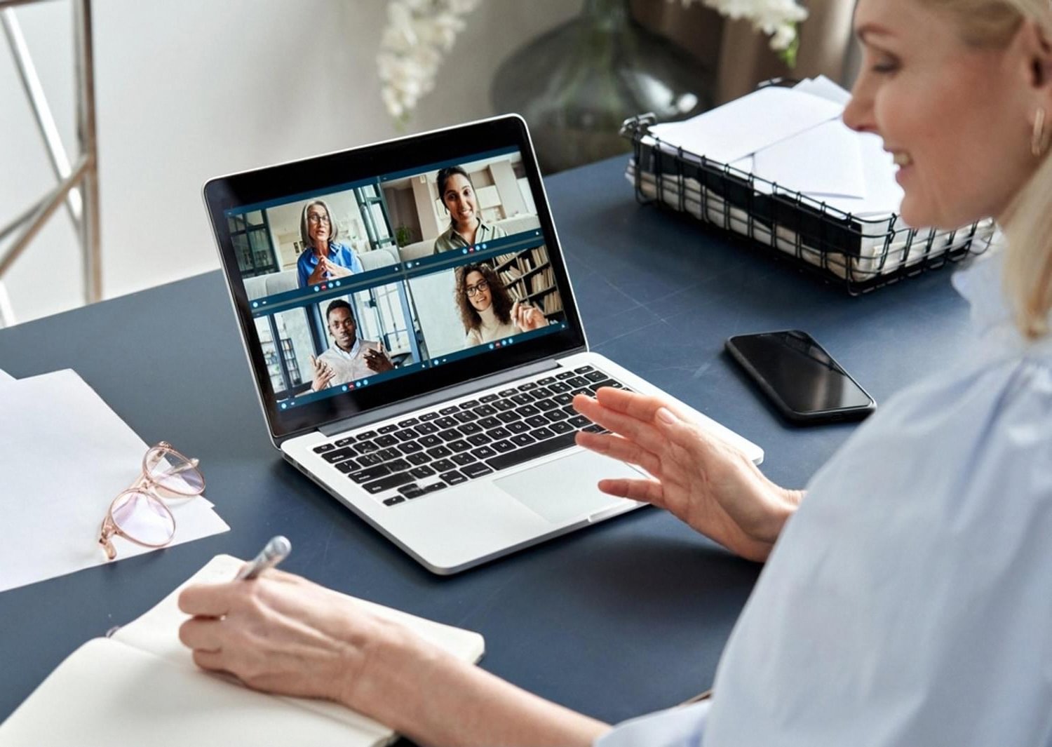 Woman taking notes during a hybrid video lesson with four classmates on screen